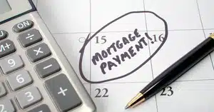 Close-up of a calendar with the 15th circled and labeled 'Mortgage Payment,' accompanied by a calculator and pen.