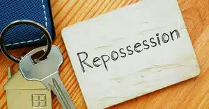 Close-up of a keychain with a house key and a wooden card with the word 'Repossession' written on it.